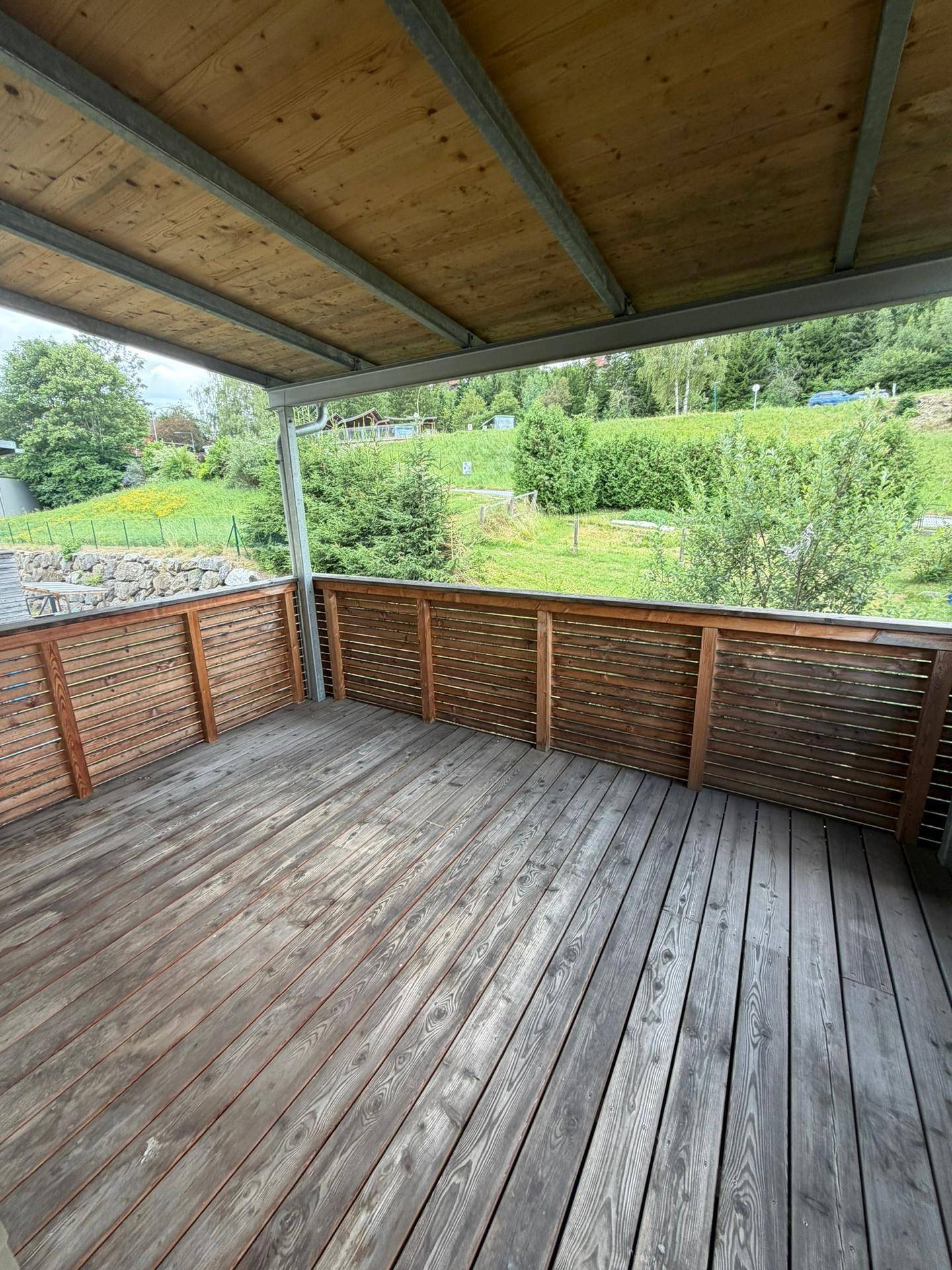 Geräumiger überdachter Balkon mit Holzboden und weitem Blick auf die grüne Landschaft.