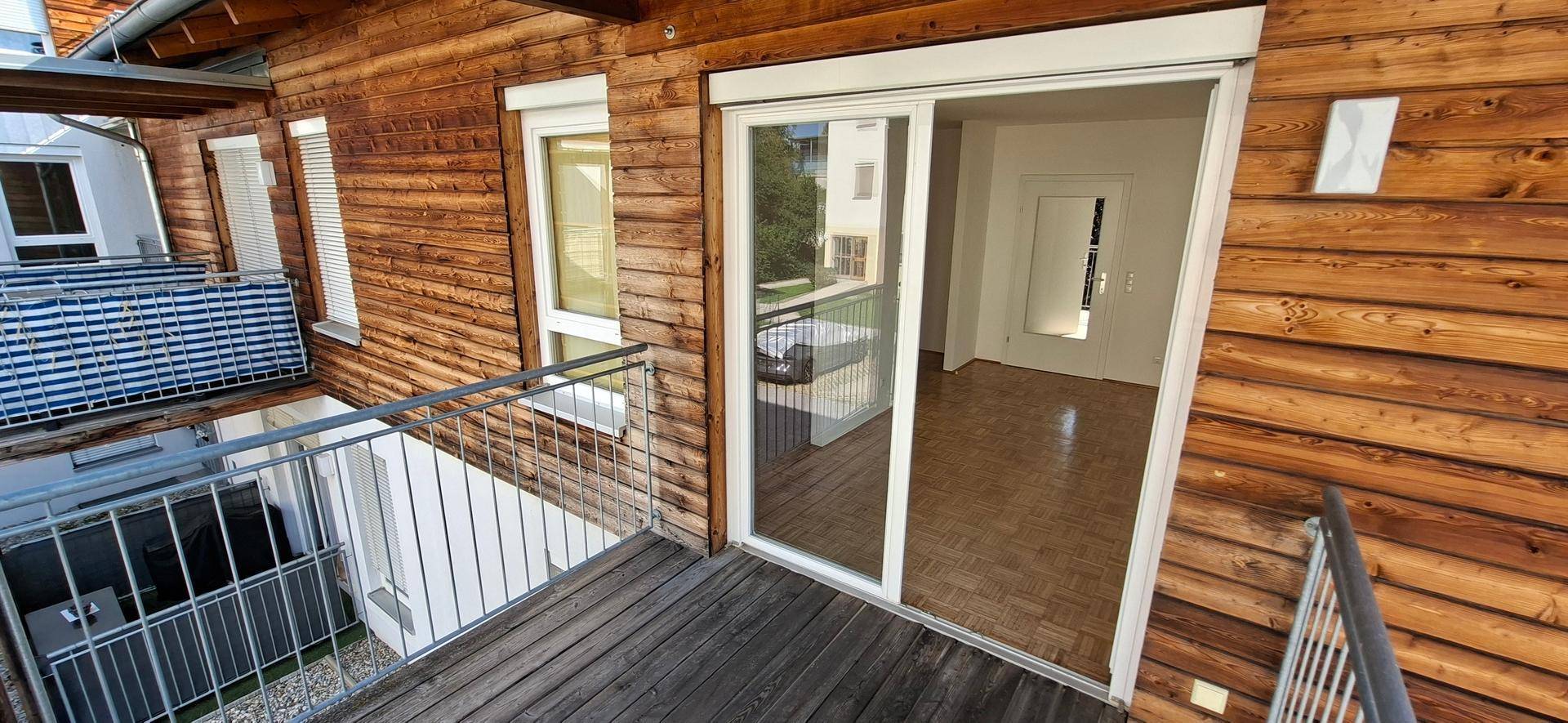Holzbalkon an der Fassade des Gebäudes mit Schiebetür, die in einen hellen Innenraum führt.