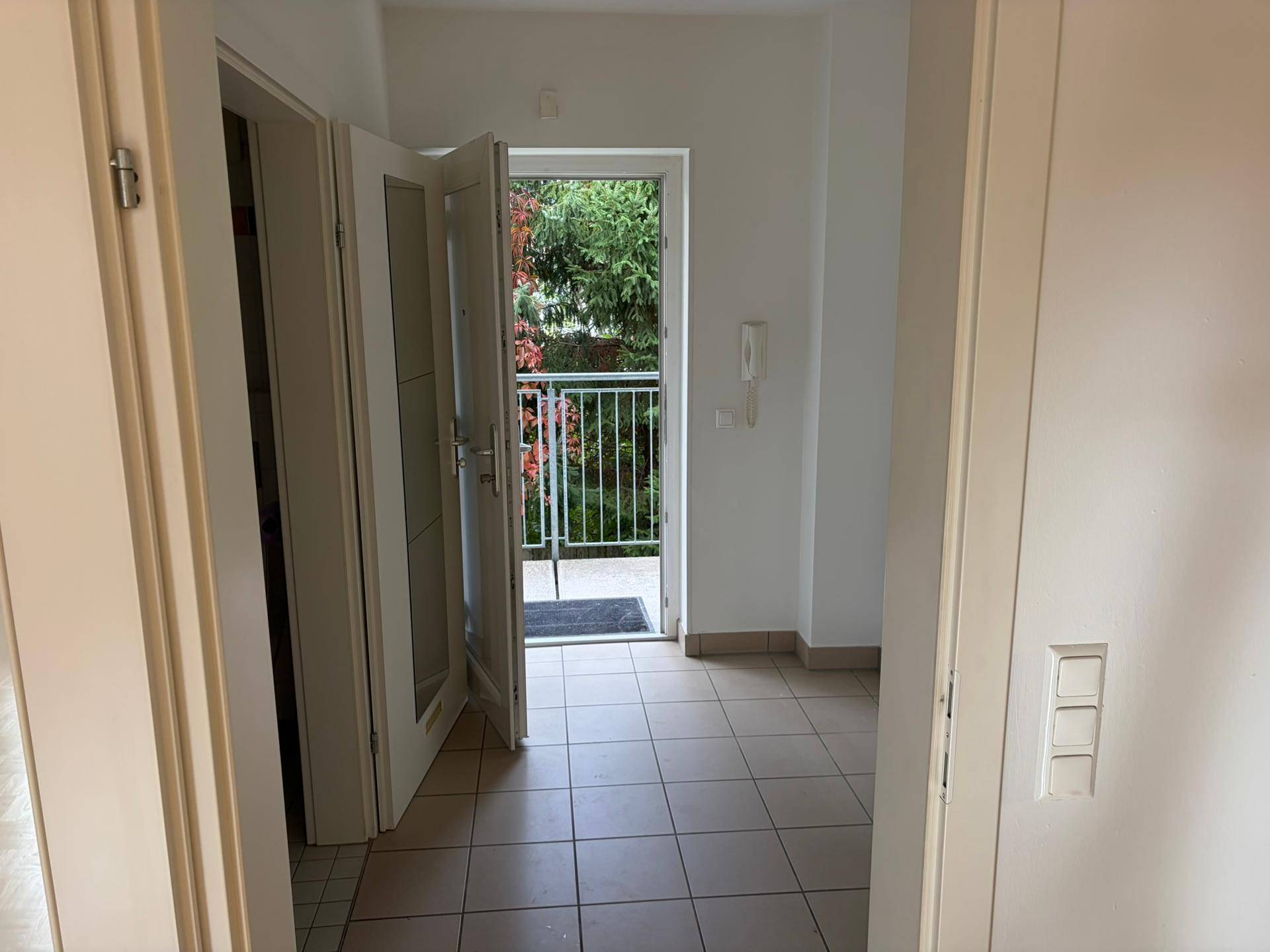 Heller Eingangsbereich mit Fliesenboden und offener Tür, die zu einem kleinen Balkon führt.