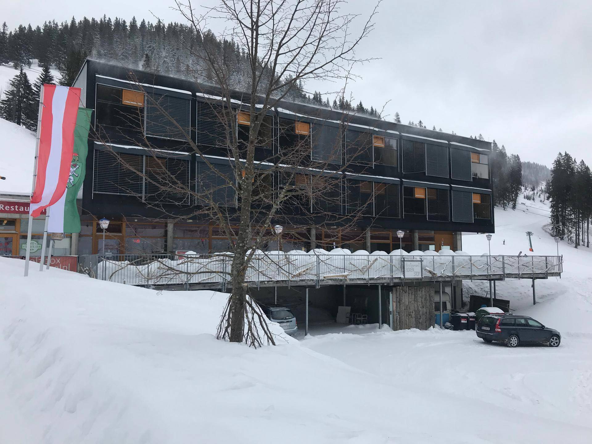 Winteransicht des modernen Gebäudes mit schwarzer Fassade, umgeben von Schnee und Bäumen.