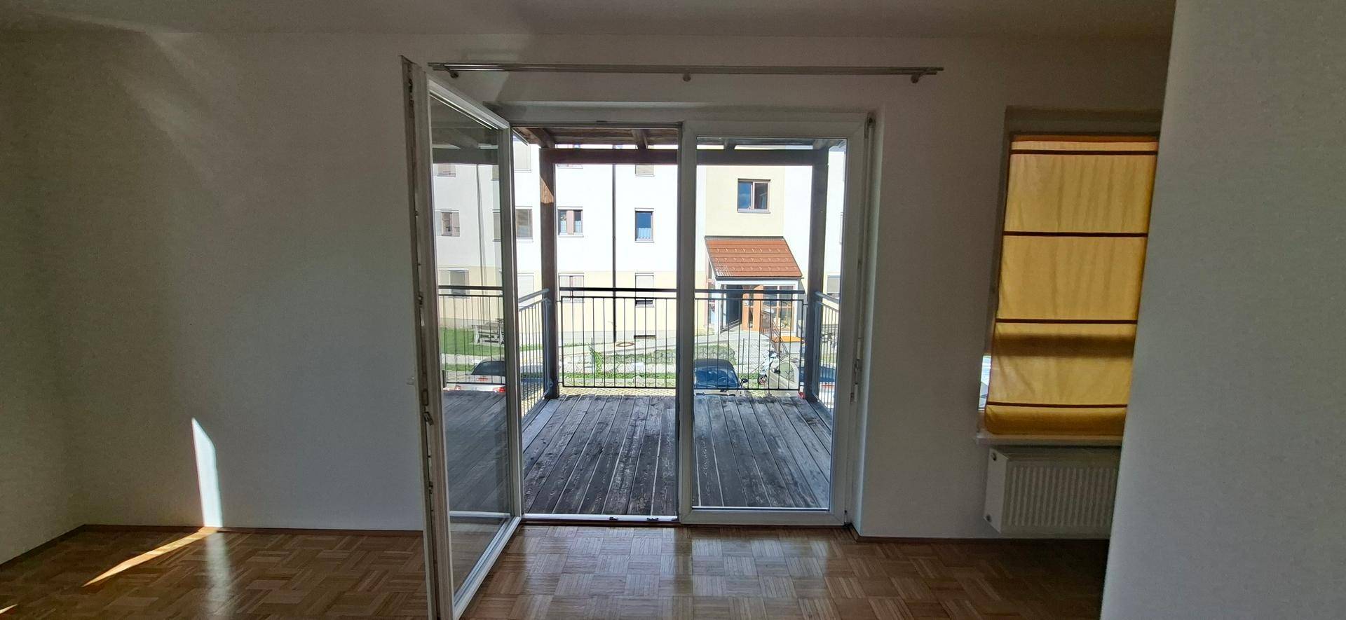 Heller Wohnraum mit Parkettboden und großem Schiebefenster, das Zugang zu einem Balkon bietet.