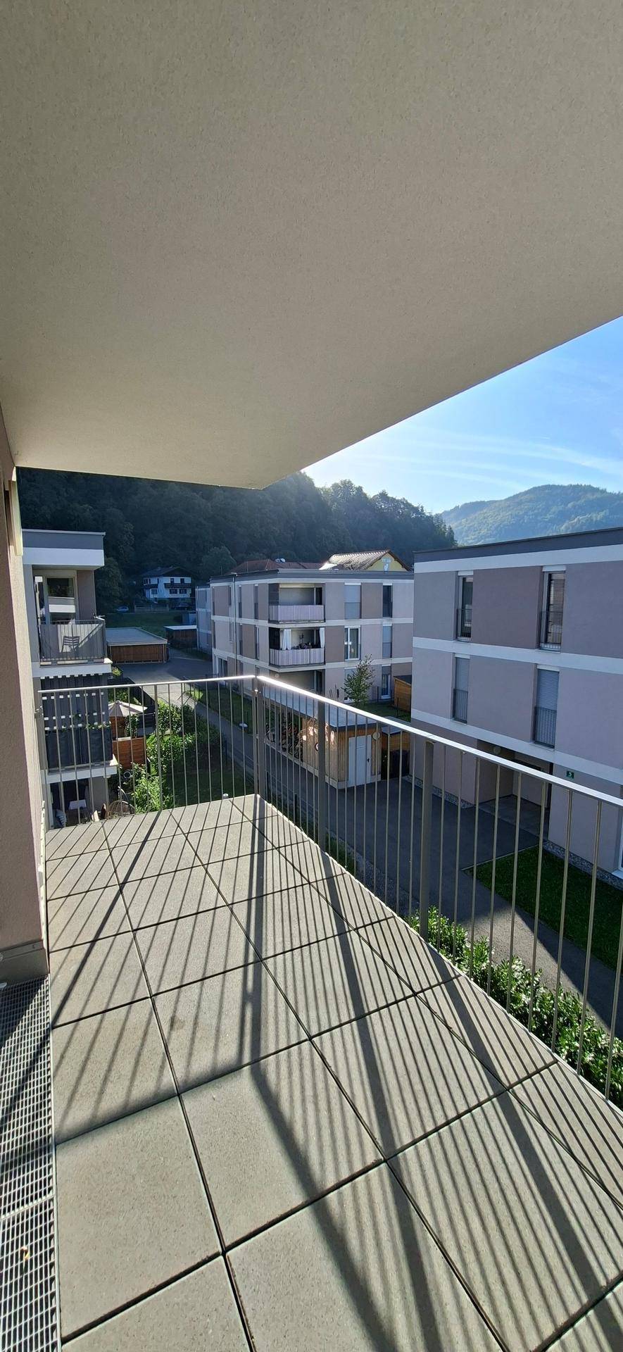 Sonniger Balkon mit Fliesenboden und weitem Blick auf die umliegende Wohnbebauung und Berge.