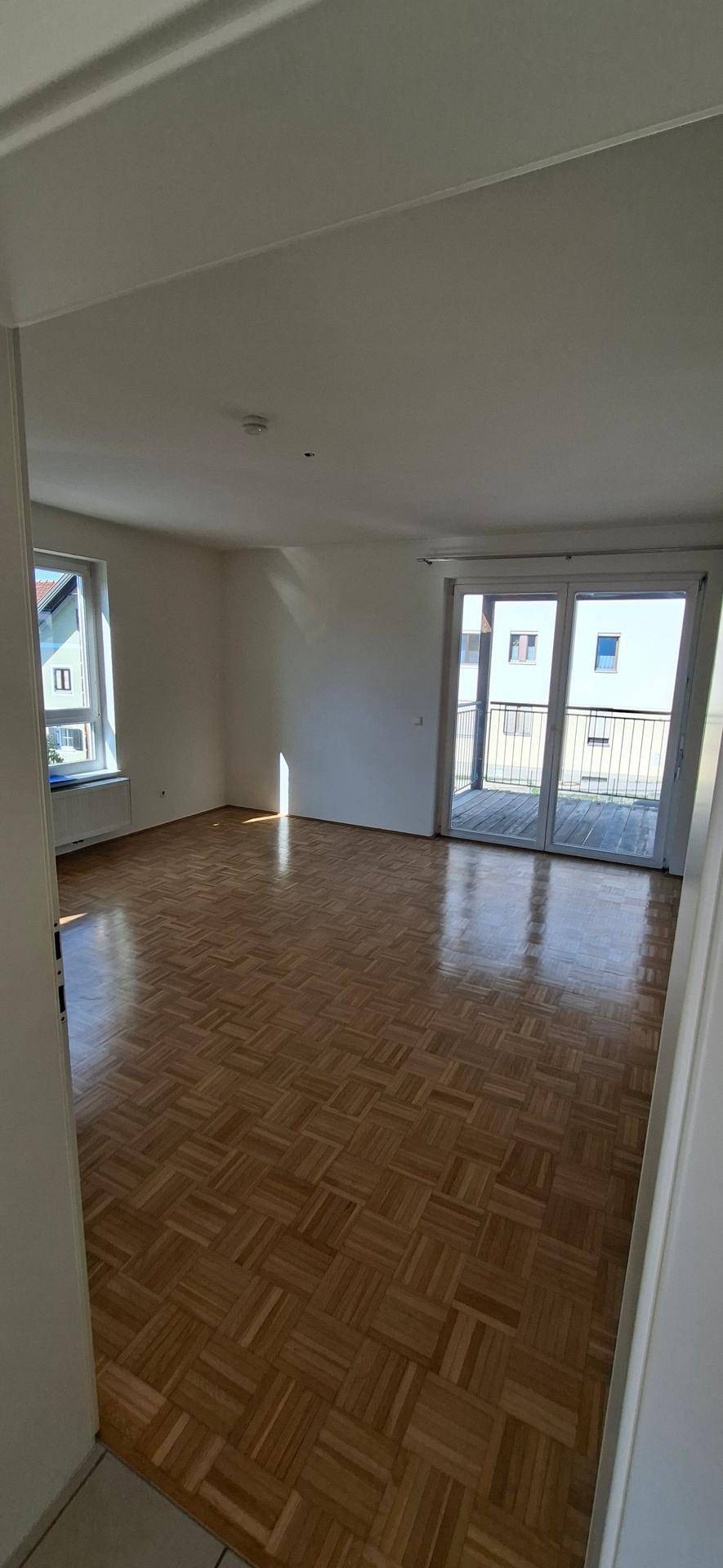 Blick vom Flur in das helle Wohnzimmer mit Parkettboden und Zugang zum Balkon.