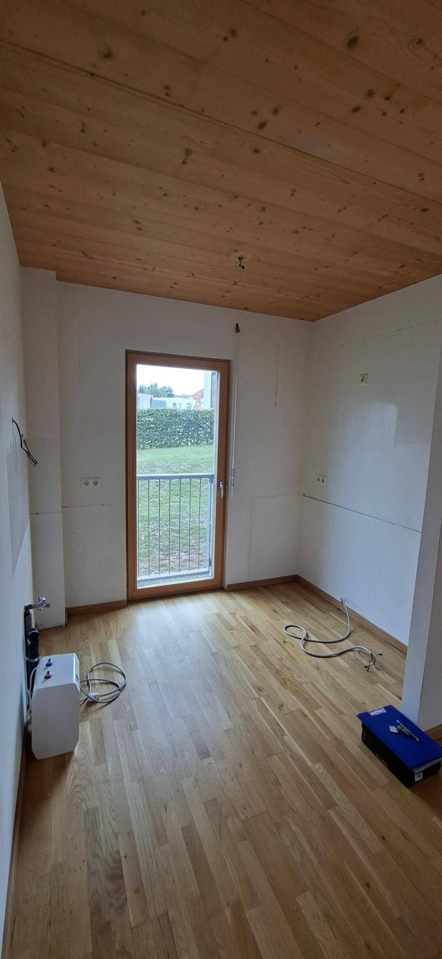 Leere Küche mit Holzboden und Holzdecke, vorbereitet für die Installation einer Einbauküche.