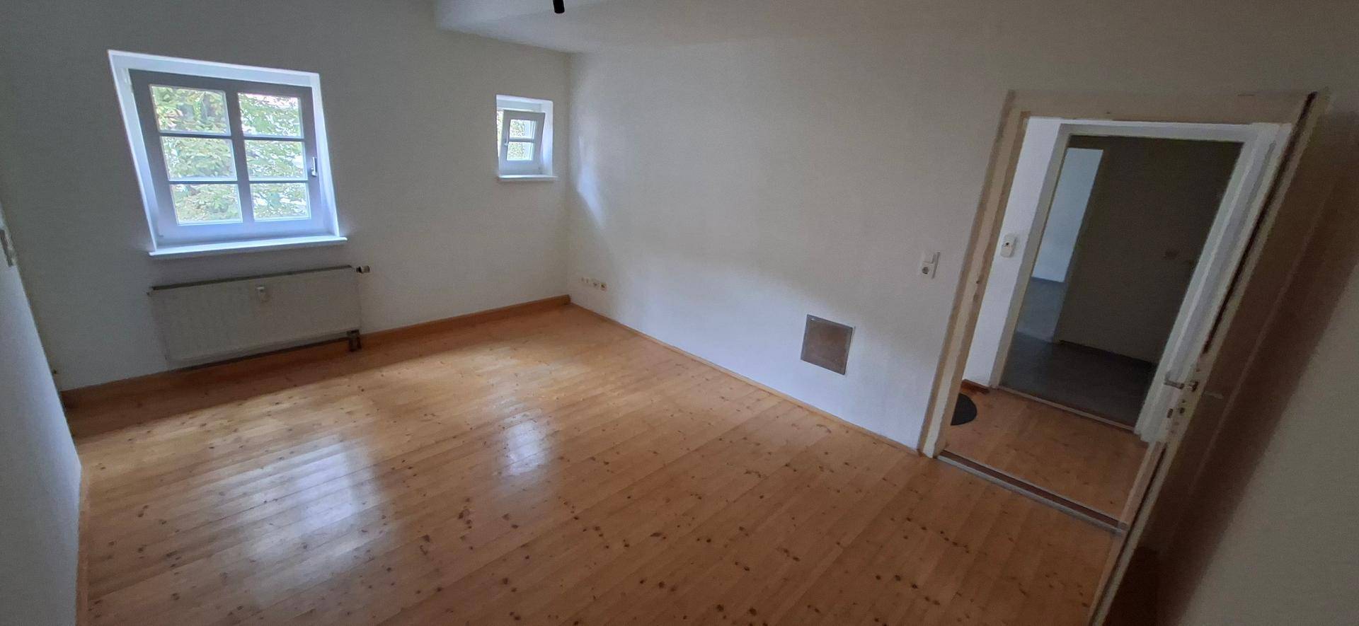 Heller Wohnraum mit Holzplankenboden und zwei Fenstern, die für eine angenehme Atmosphäre sorgen.