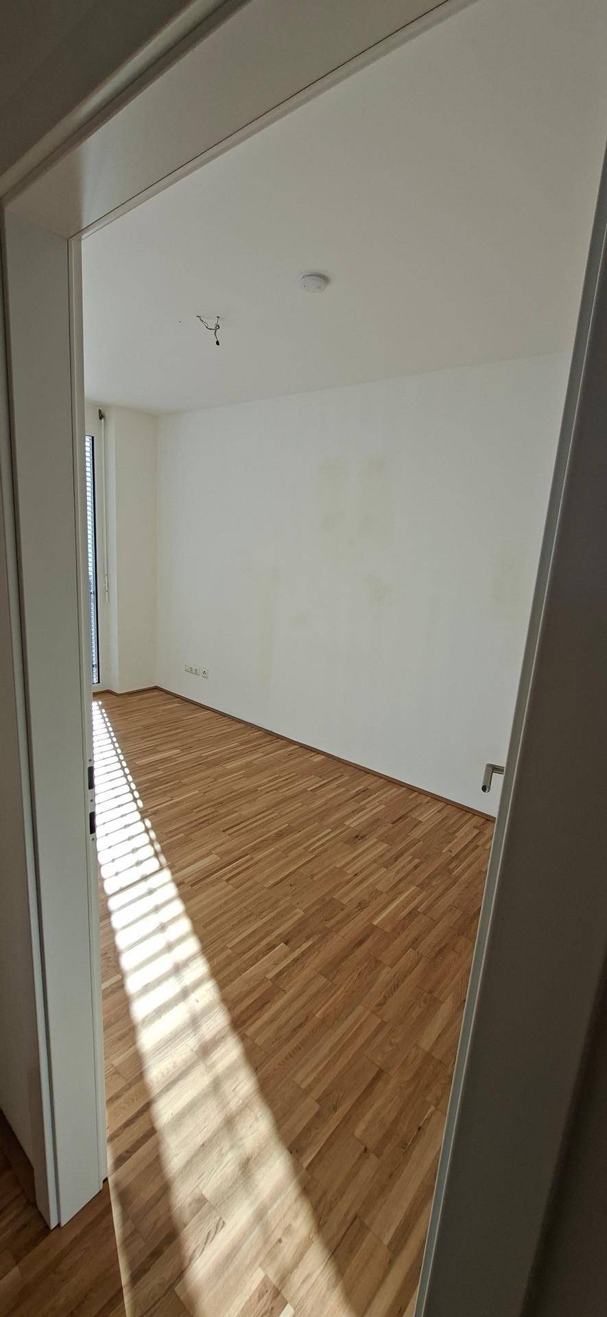 Helles Schlafzimmer mit Holzparkettboden und großen Fenstern, die viel Sonnenlicht hereinlassen.