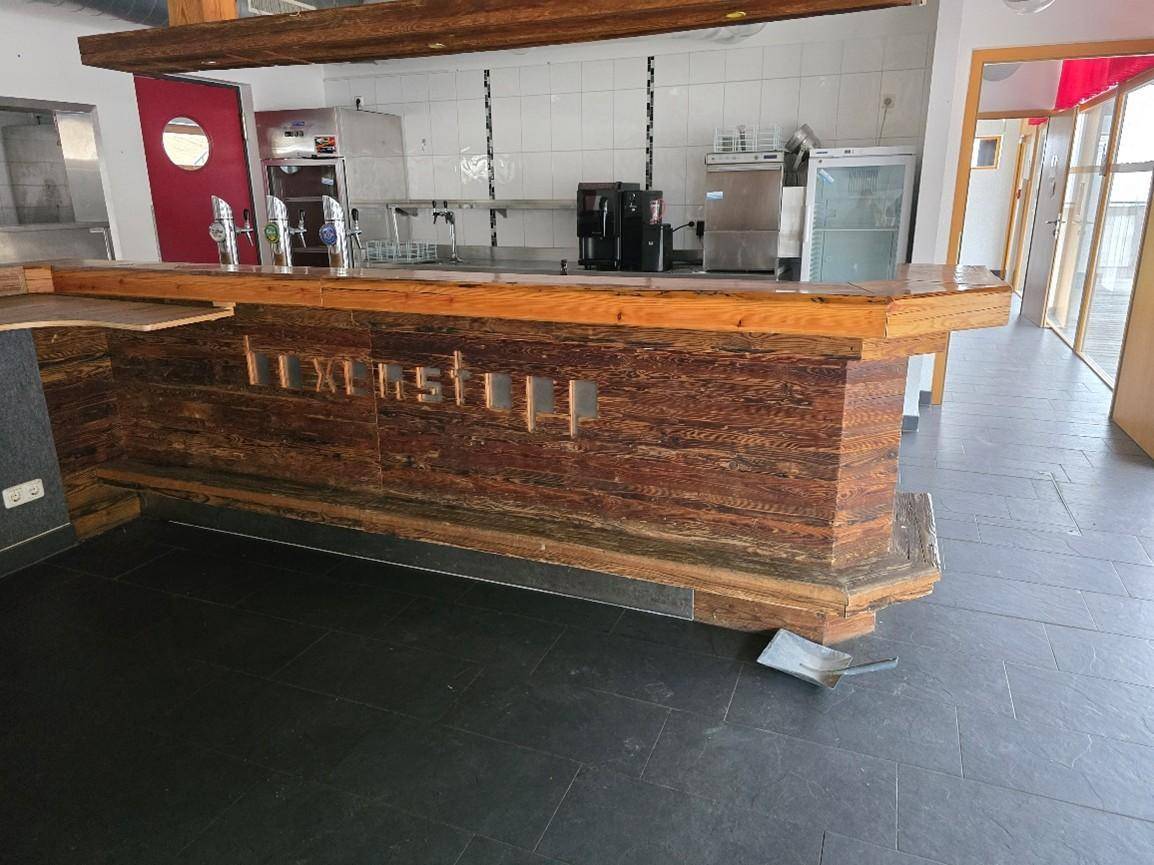 Bar mit rustikaler Holztheke, dunklen Fliesen und professioneller Ausstattung im Hintergrund.