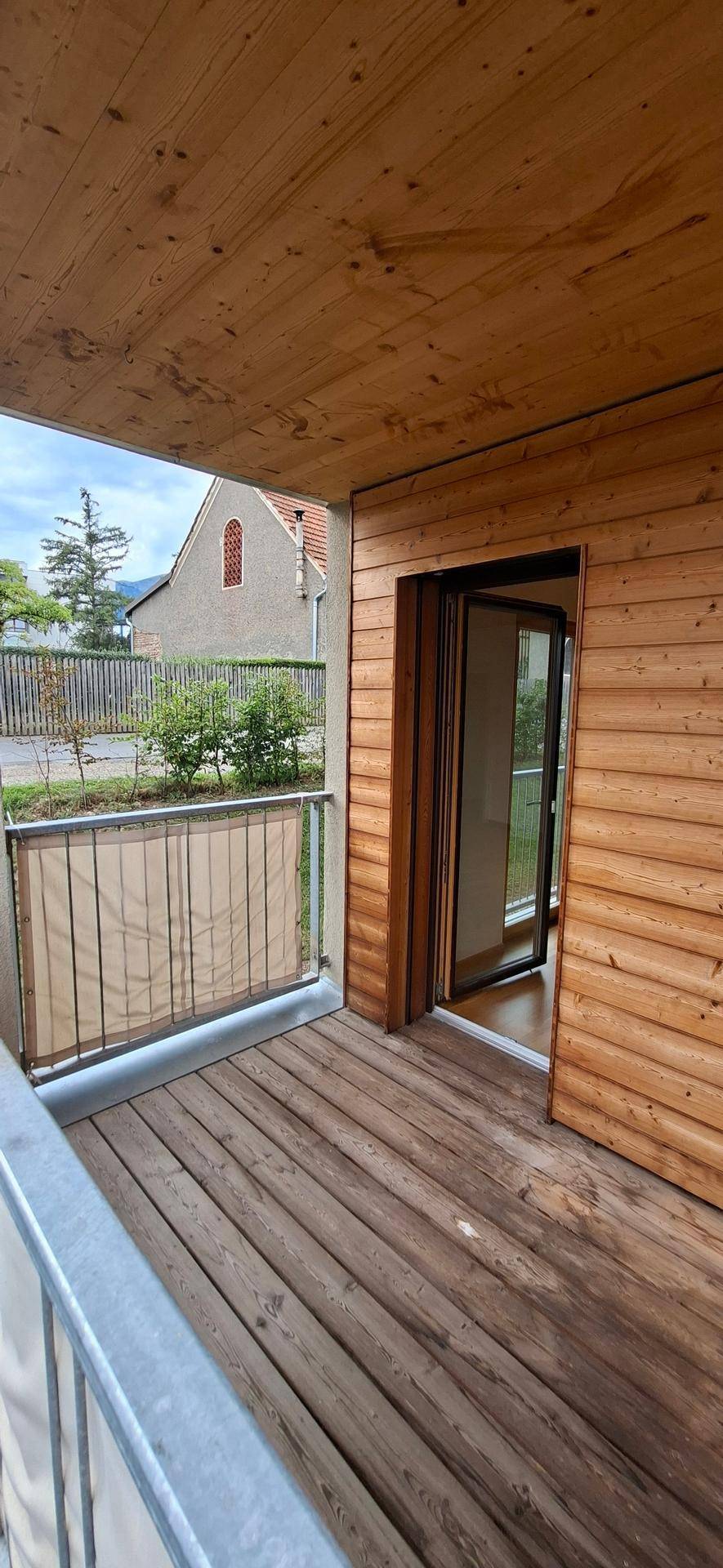 Holzverkleideter Balkon mit Holzboden und Blick auf die ruhige Wohngegend.