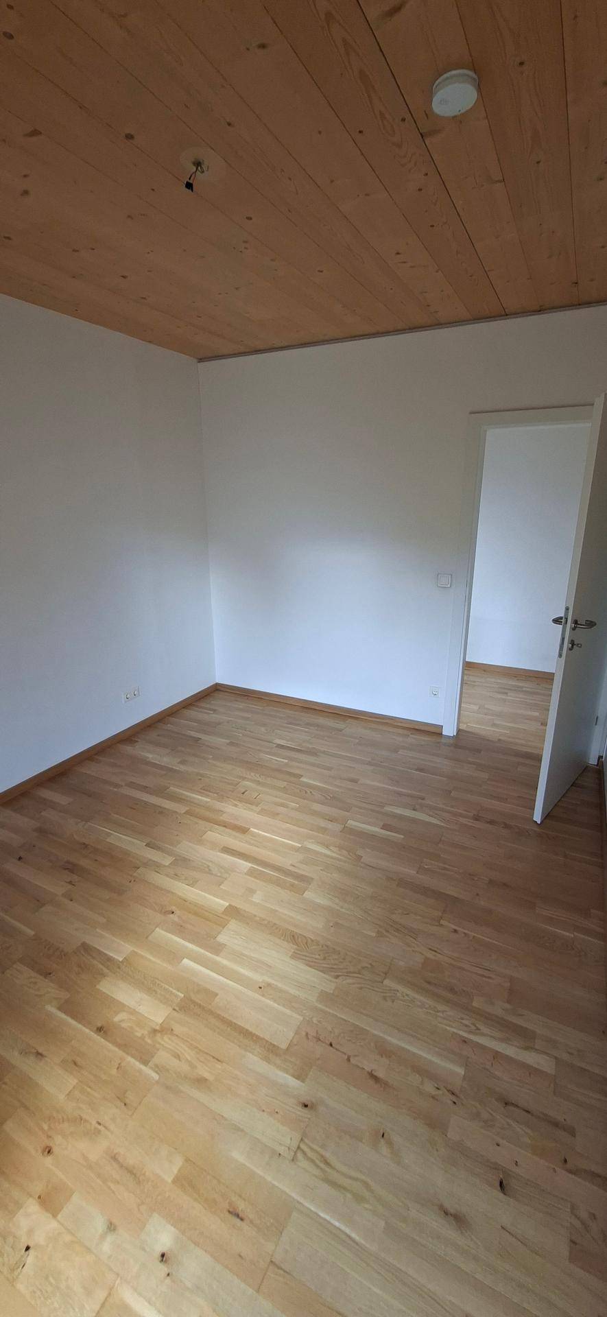 Geräumiges, leeres Zimmer mit hellem Holzboden und Holzdecke, ideal als Schlafzimmer.