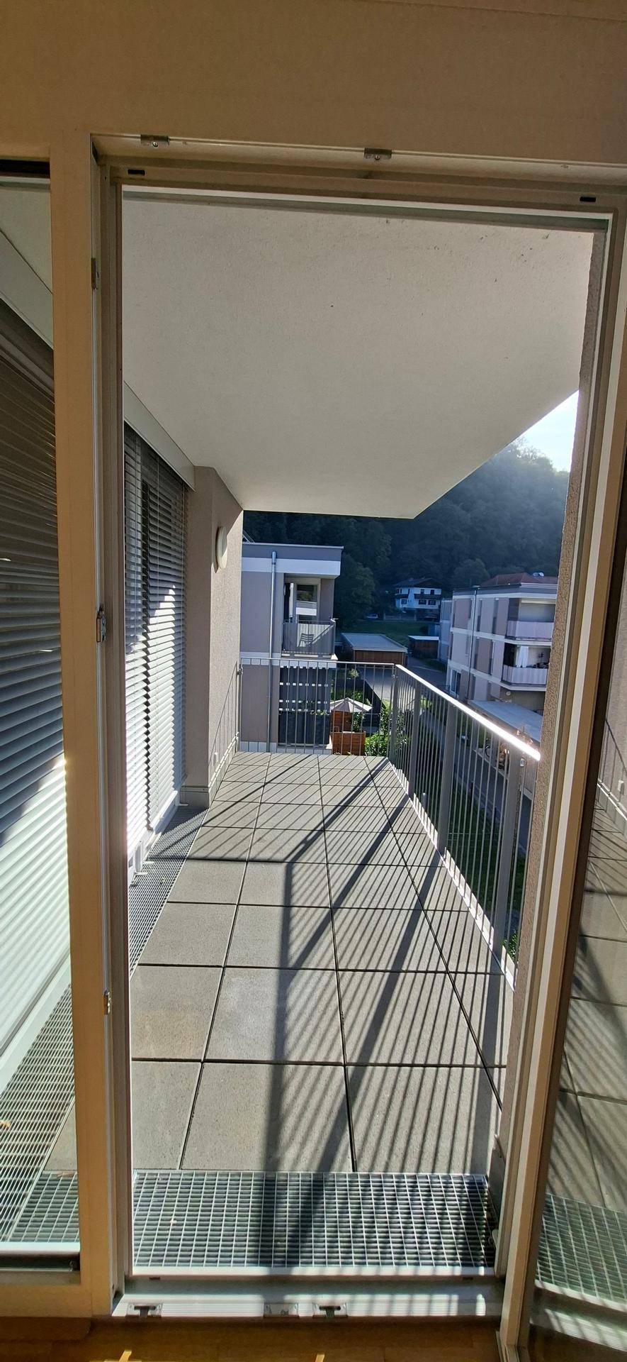 Heller Balkon mit Fliesenboden und Blick auf die umliegenden Gebäude und Berge.