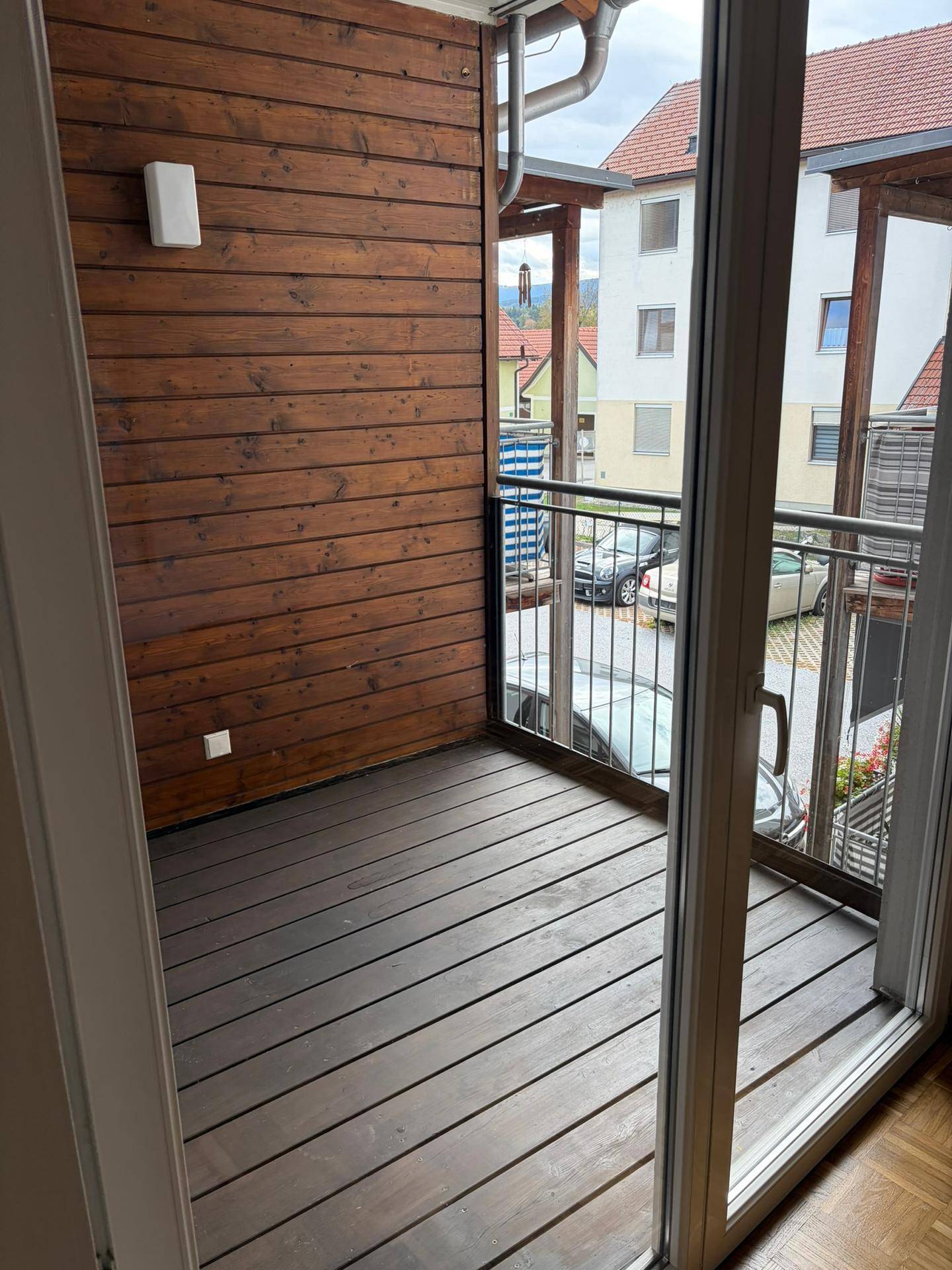 Gemütlicher Balkon mit Holzverkleidung und Holzboden, bietet einen Blick auf die umliegenden Gebäude.