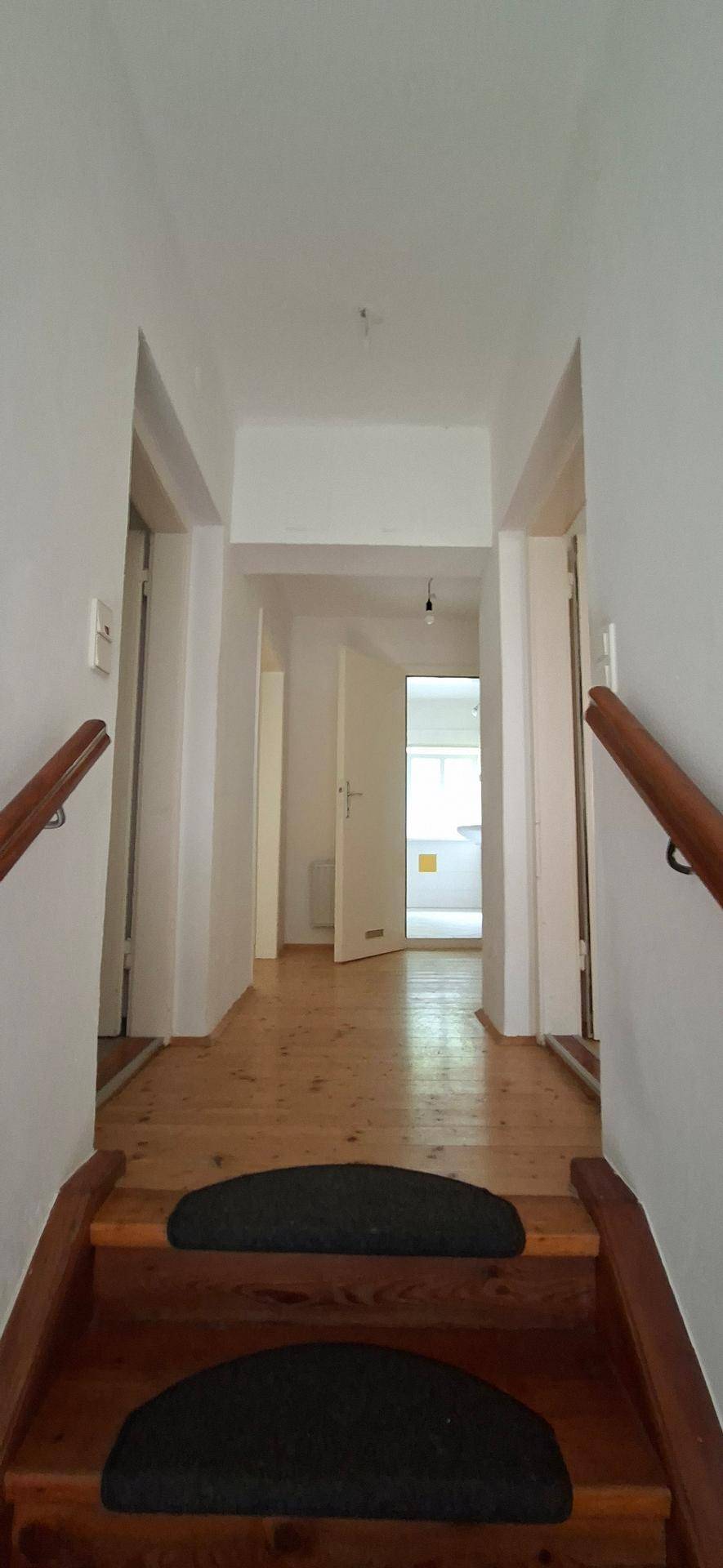Oberer Treppenabsatz mit Holzfußboden und Blick in einen hellen Flur mit mehreren Türen.