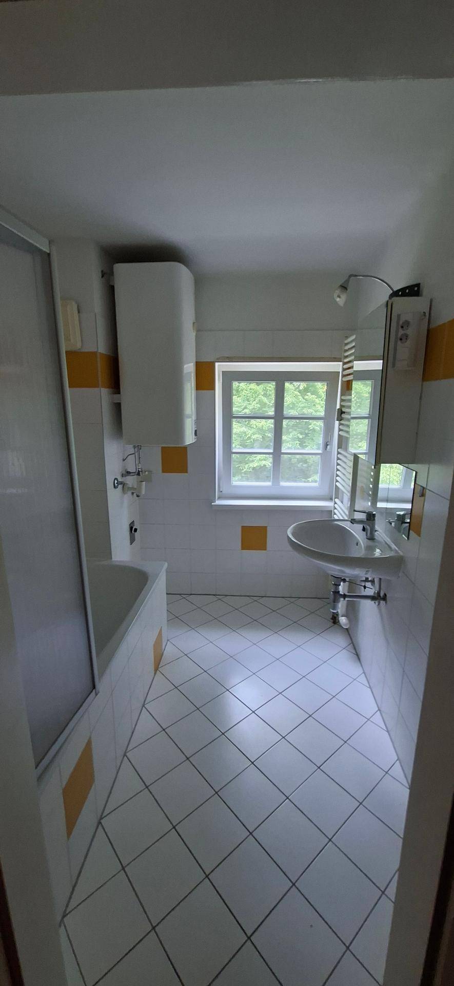 Helles Badezimmer mit weißen Fliesen, Badewanne mit Duschfunktion und Fenster.