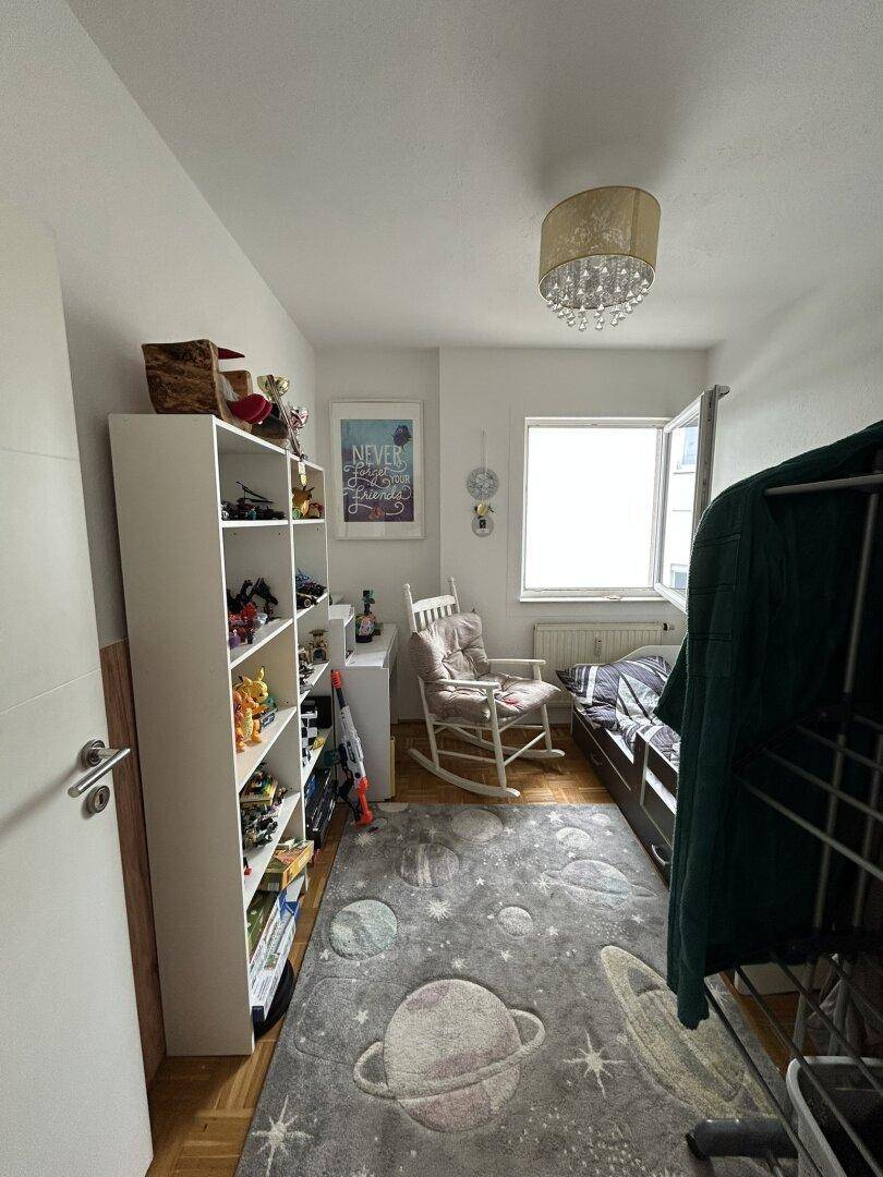 Helles Kinderzimmer mit Schaukelstuhl, Stauraum und Blick nach draußen.