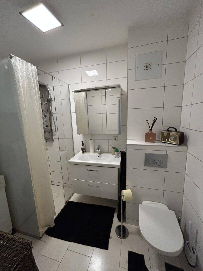 Modern gefliestes Badezimmer mit Dusche, wandhängendem WC und Einzelwaschbecken.