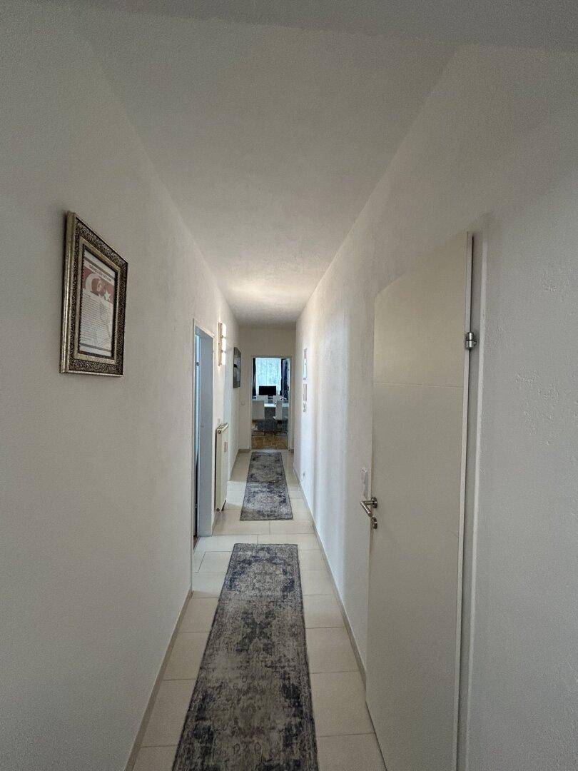 Langer, heller Flur mit Fliesenboden und Bildern an der Wand, der zu weiteren Räumen führt.