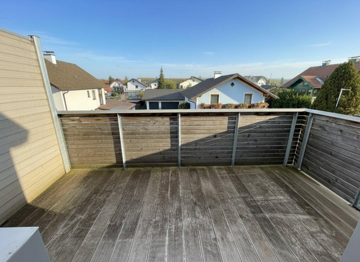 Geräumige Holzterrasse mit Blick auf die umliegenden Häuser und die Landschaft.
