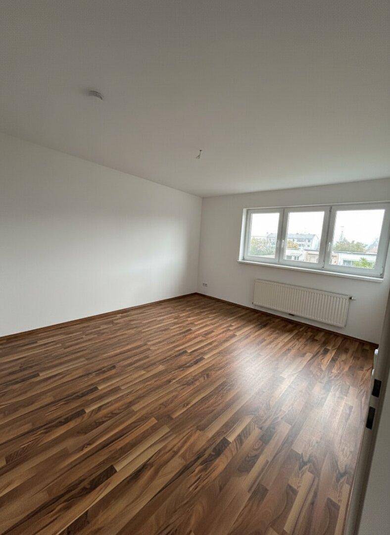 Leeres Zimmer mit Holzboden und Fenster, ideal als Schlaf- oder Kinderzimmer.