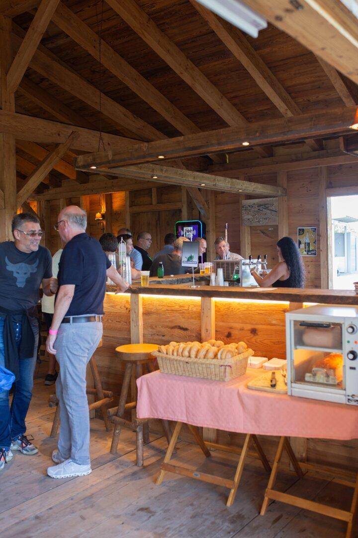 Barbereich mit Gästen, Holztresen und Snacks, lebhafte Atmosphäre.