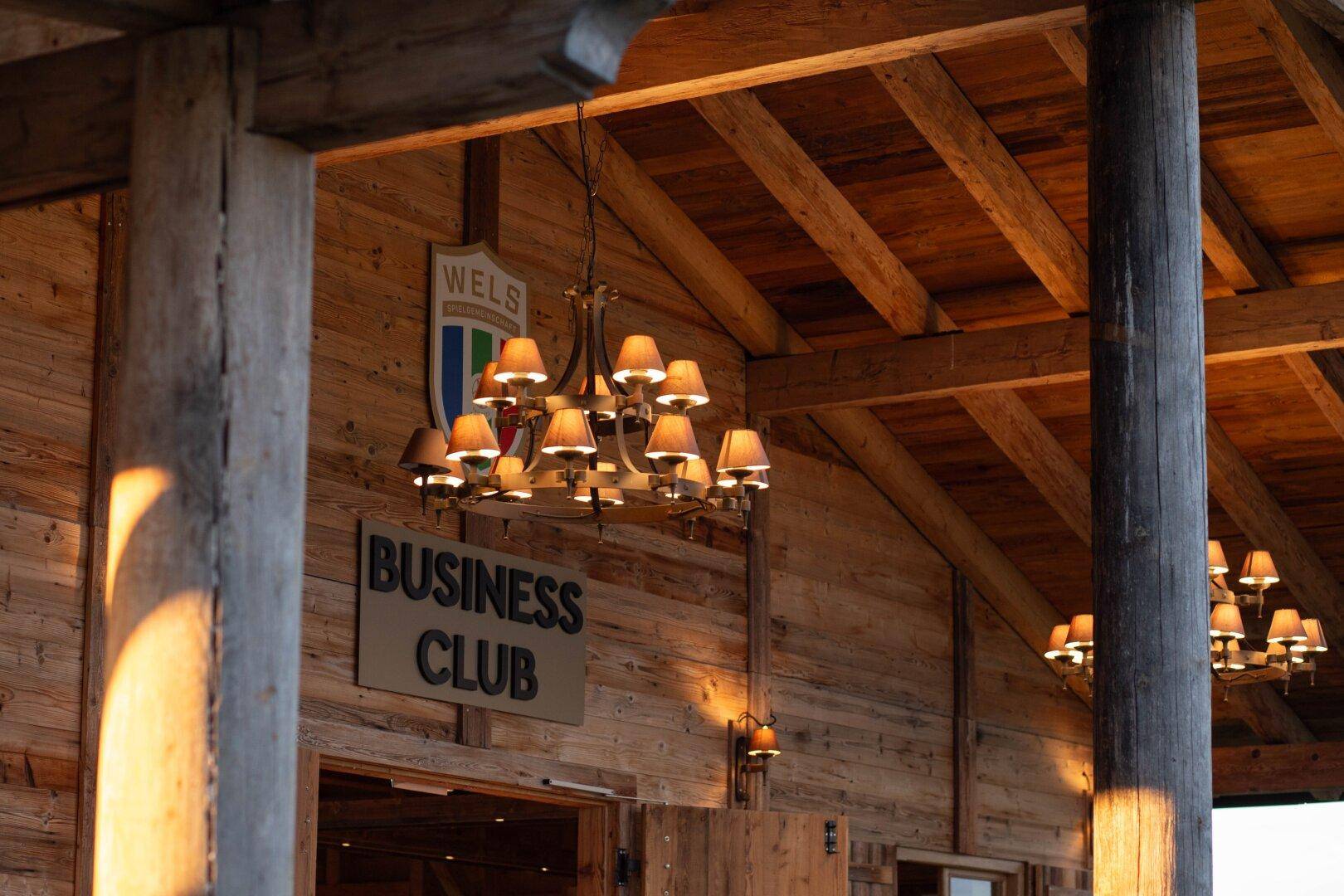 Eingangsbereich des Holzgebäudes mit Kronleuchtern und einem "Business Club" Schild.