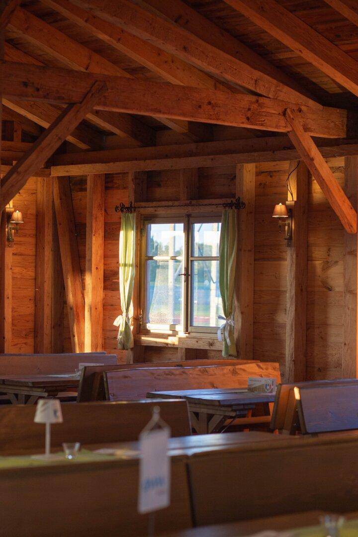Sonnenlicht fällt durch die Fenster auf die Holzbänke und Tische im rustikalen Festsaal.