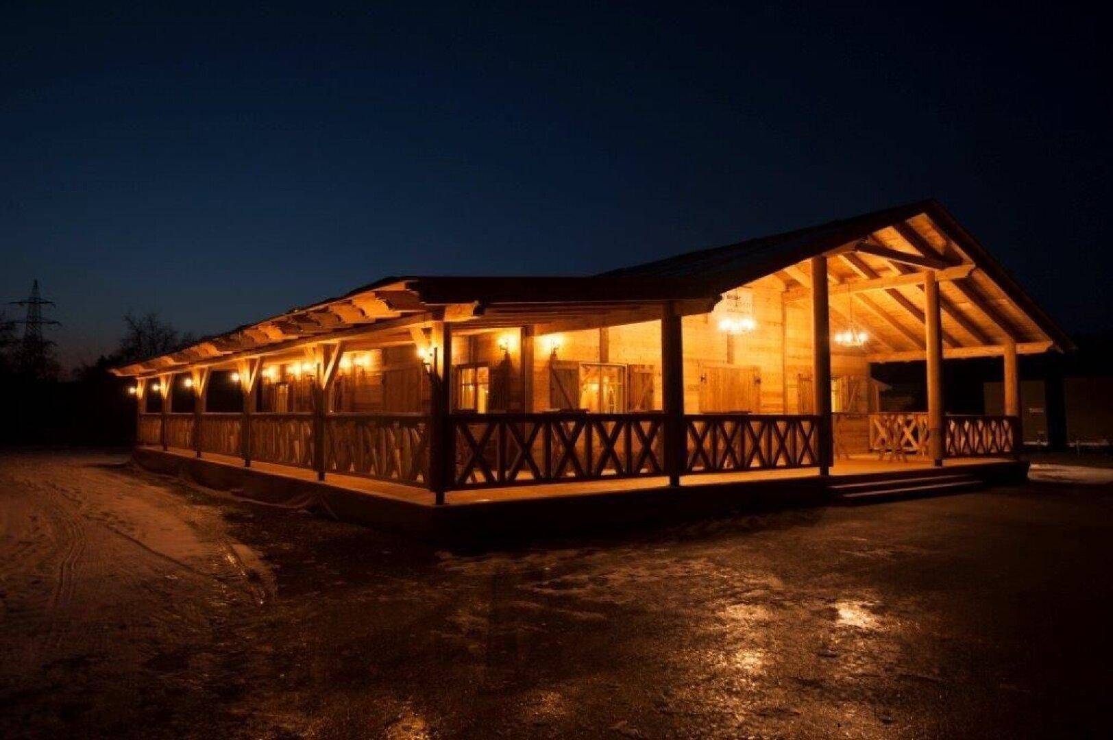 Langes Holzgebäude mit beleuchteter Veranda bei Nacht, umgeben von dunkler Landschaft.