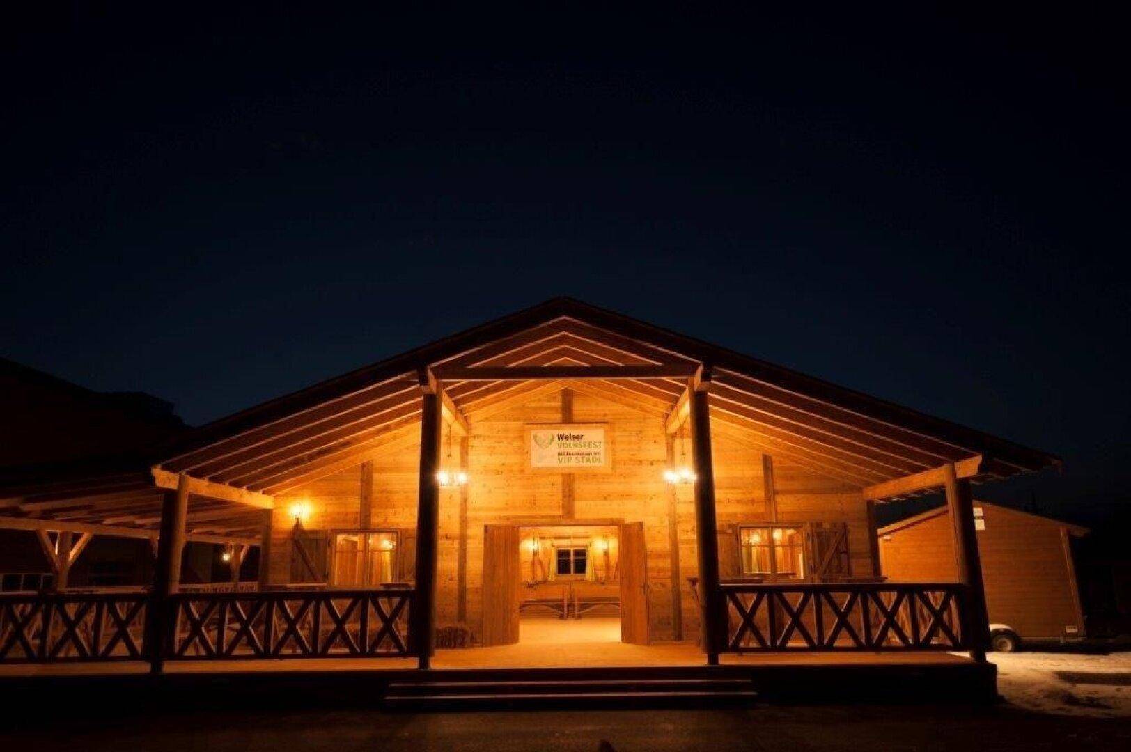 Rustikales Holzgebäude bei Nacht, beleuchtet mit warmen Lichtern, einladend für Gäste.