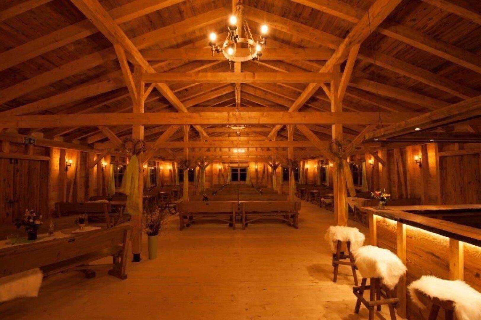 Geräumiger Festsaal mit Holzbalken und langen Holzbänken, warm beleuchtet für eine Veranstaltung.