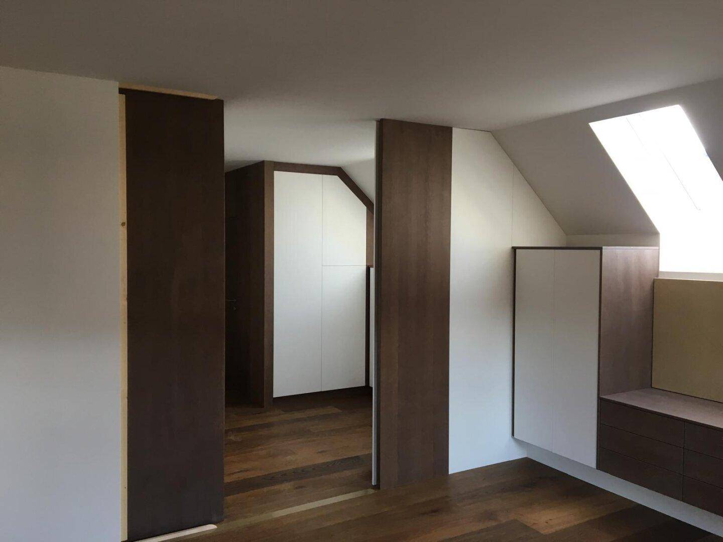 Geräumiger Raum mit maßgefertigten Einbauschränken und Holzfußboden unter der Dachschräge.