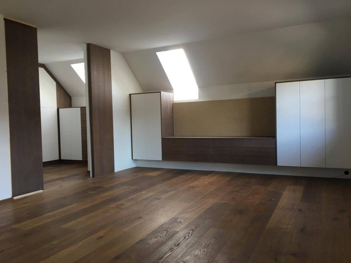 Großzügiger Raum mit Holzfußboden, Einbaumöbeln und Dachfenstern unter der Dachschräge.