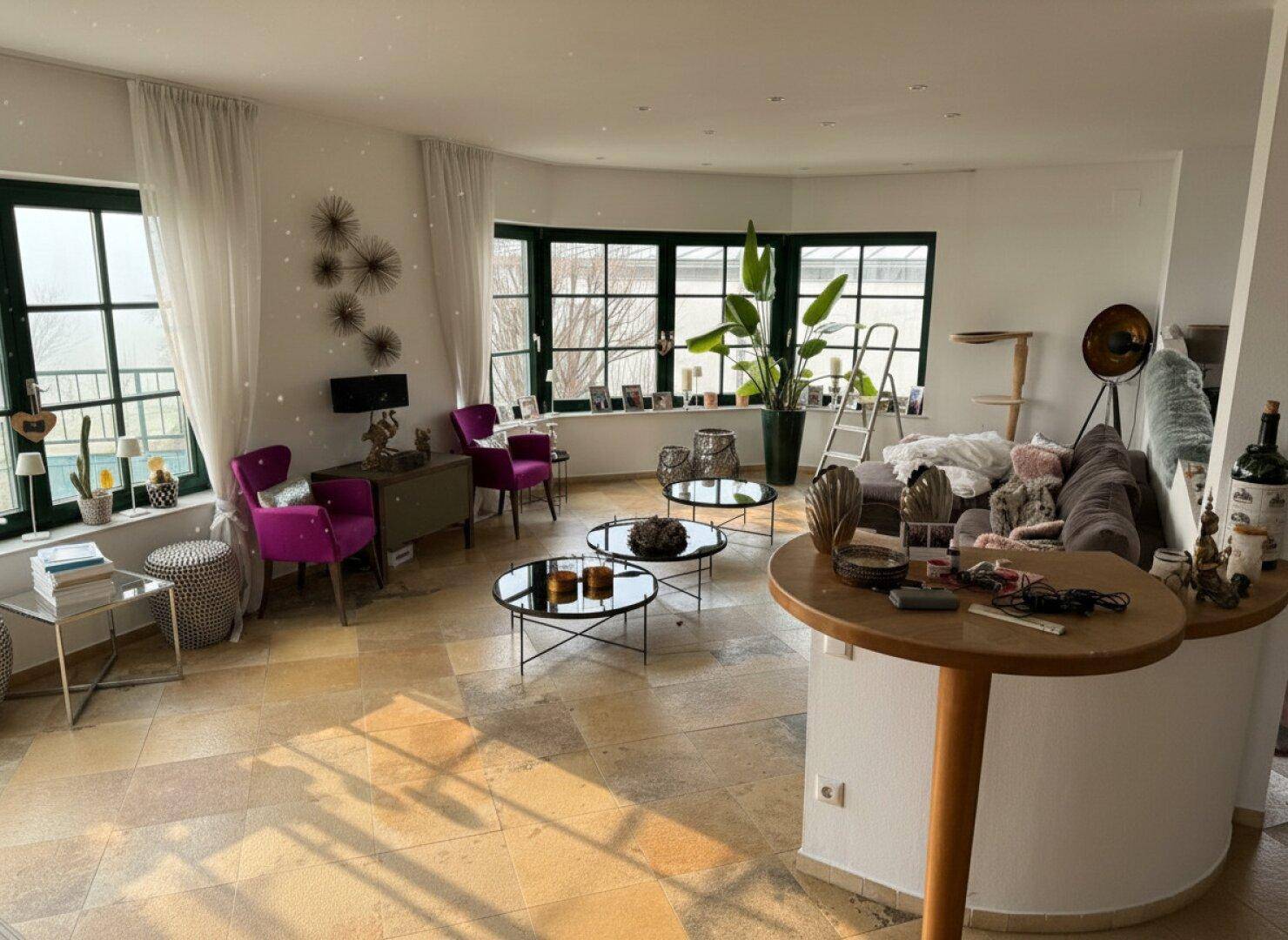 Helles und geräumiges Wohnzimmer mit großen Fenstern, Steinboden und moderner Dekoration.