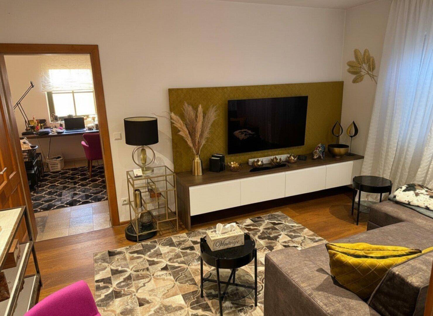 Gemütliches Wohnzimmer mit modernem TV-Möbel, bequemer Couch und Zugang zum Arbeitszimmer.