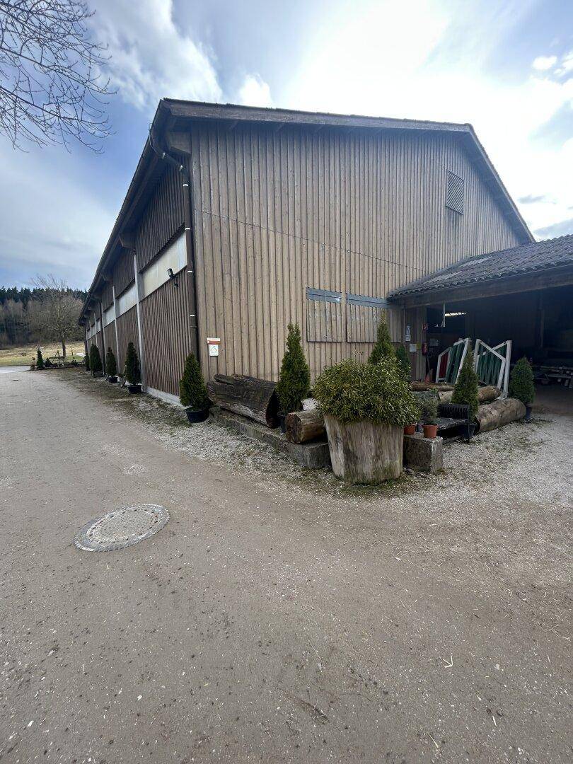 Rustikales Stallgebäude mit Holzverkleidung und einem breiten Dachüberstand, umgeben von Schotter.