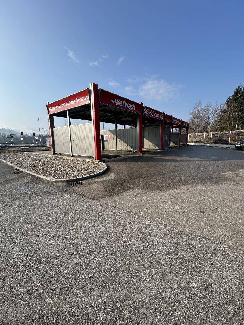 Gesamtansicht der SB-Waschanlage mit mehreren leeren Waschboxen und großzügiger asphaltierter Fläche.
