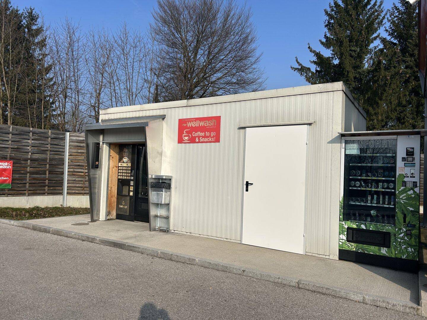 Kleines Servicegebäude neben der Waschanlage mit einem Verkaufsautomaten und einem Eingangsbereich.