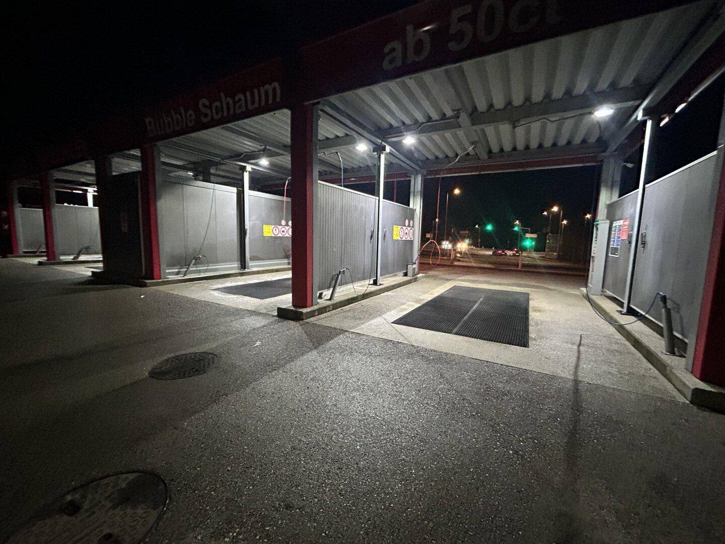 Innenansicht der beleuchteten Waschboxen der SB-Waschanlage bei Nacht, mit Blick auf die Straße im Hintergrund.
