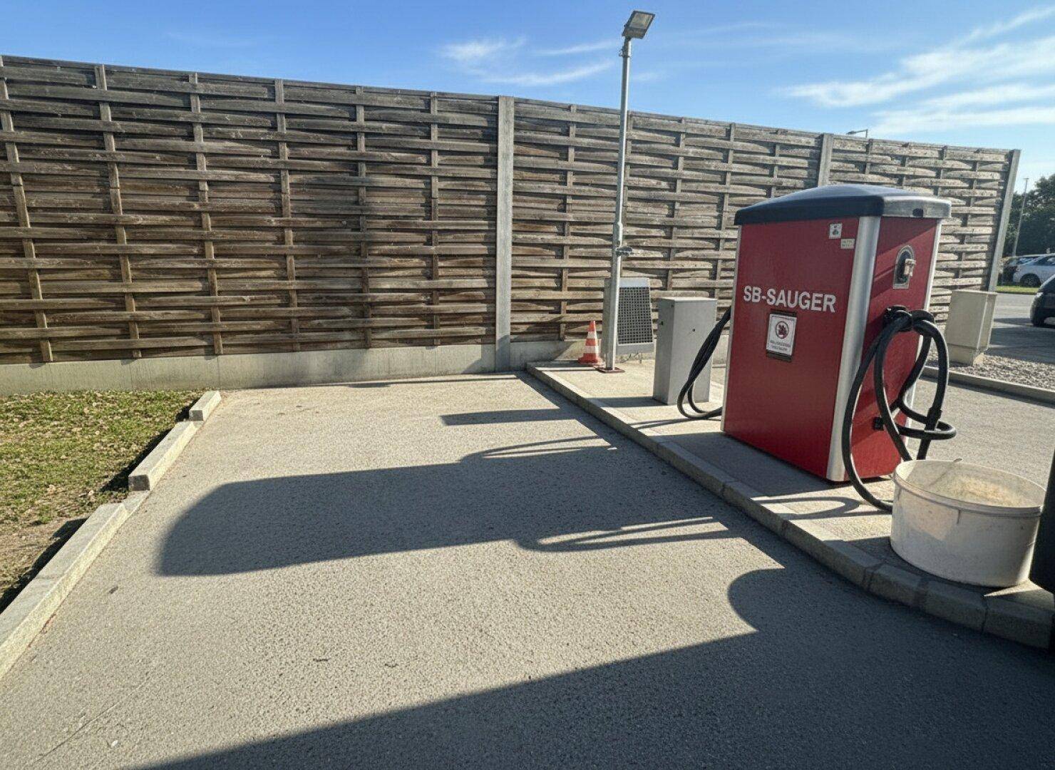 Detailansicht einer SB-Saugerstation im Außenbereich der Waschanlage, umgeben von einer hohen Holzwand.