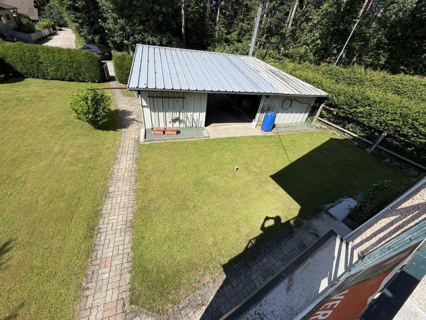 Blick von oben auf den Carport und den gepflegten Gartenbereich mit Rasenfläche.
