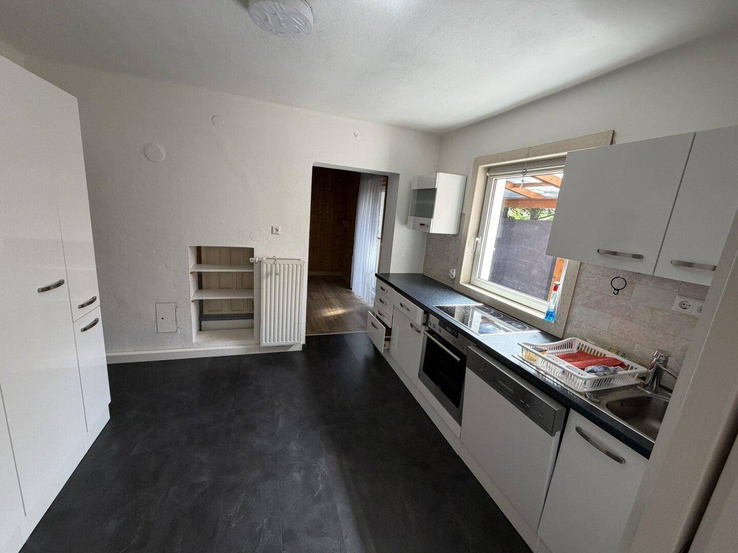 Moderne Küche mit weißen Schränken, dunkler Arbeitsplatte und integrierten Geräten.