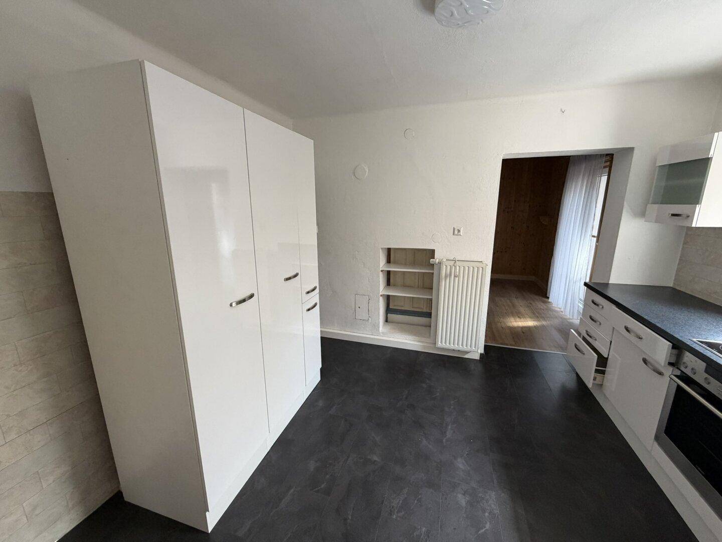 Helle Küche mit weißen Hochglanzschränken und dunklem Bodenbelag, bereit zur Nutzung.