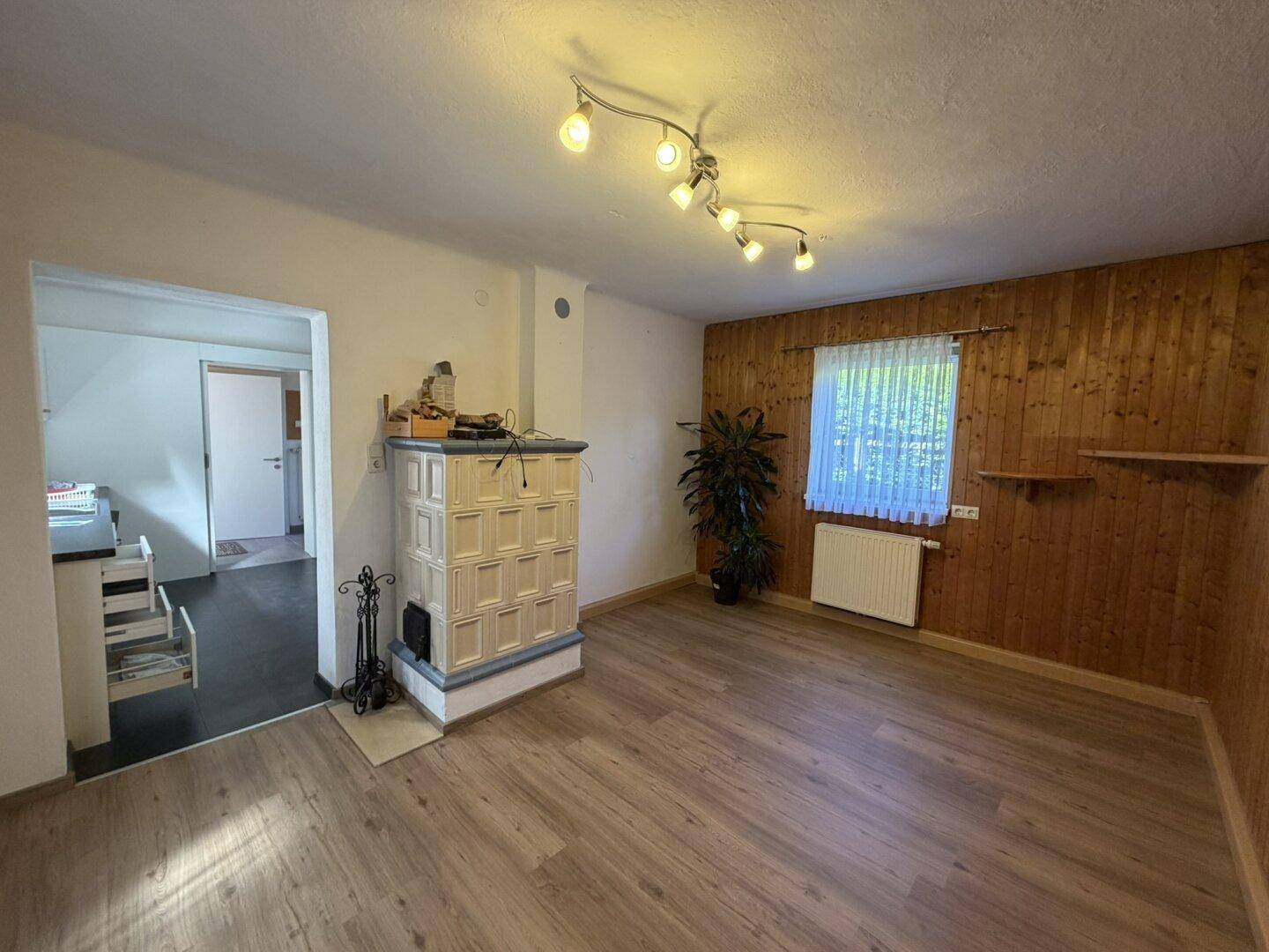 Wohnzimmer mit rustikaler Holzvertäfelung, hellem Laminatboden und einem dekorativen Kachelofen.