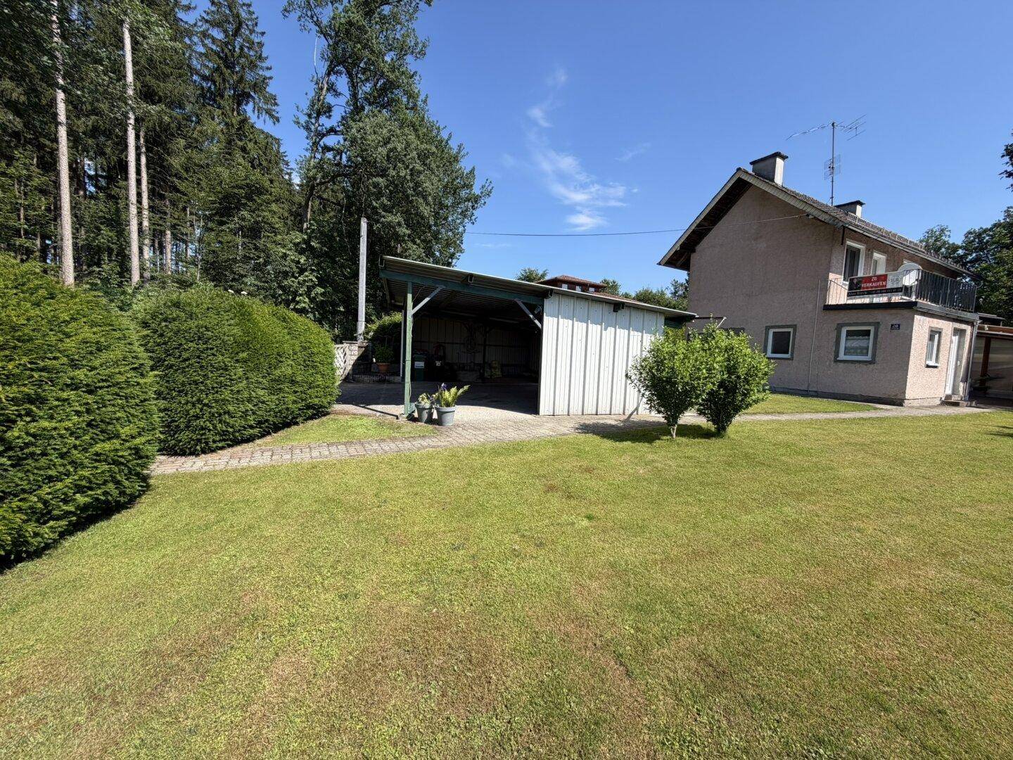 Hausansicht mit großem Rasen und Carport unter strahlend blauem Himmel.