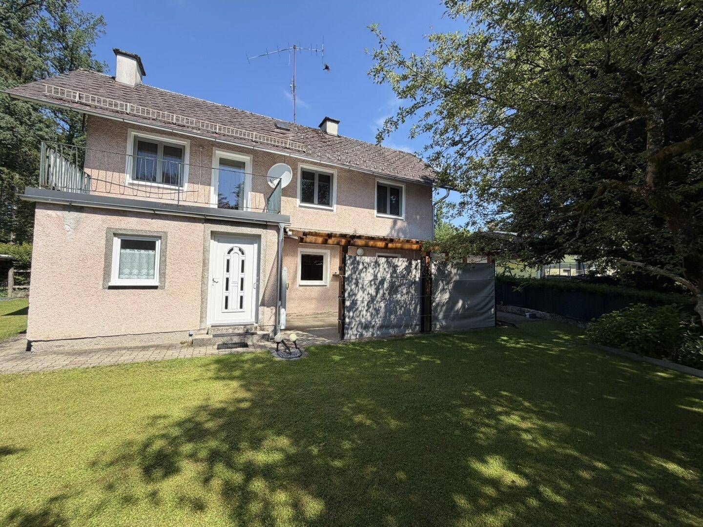 Rückansicht des Hauses mit kleinem Balkon, Zugang zum Garten und Rasenfläche.