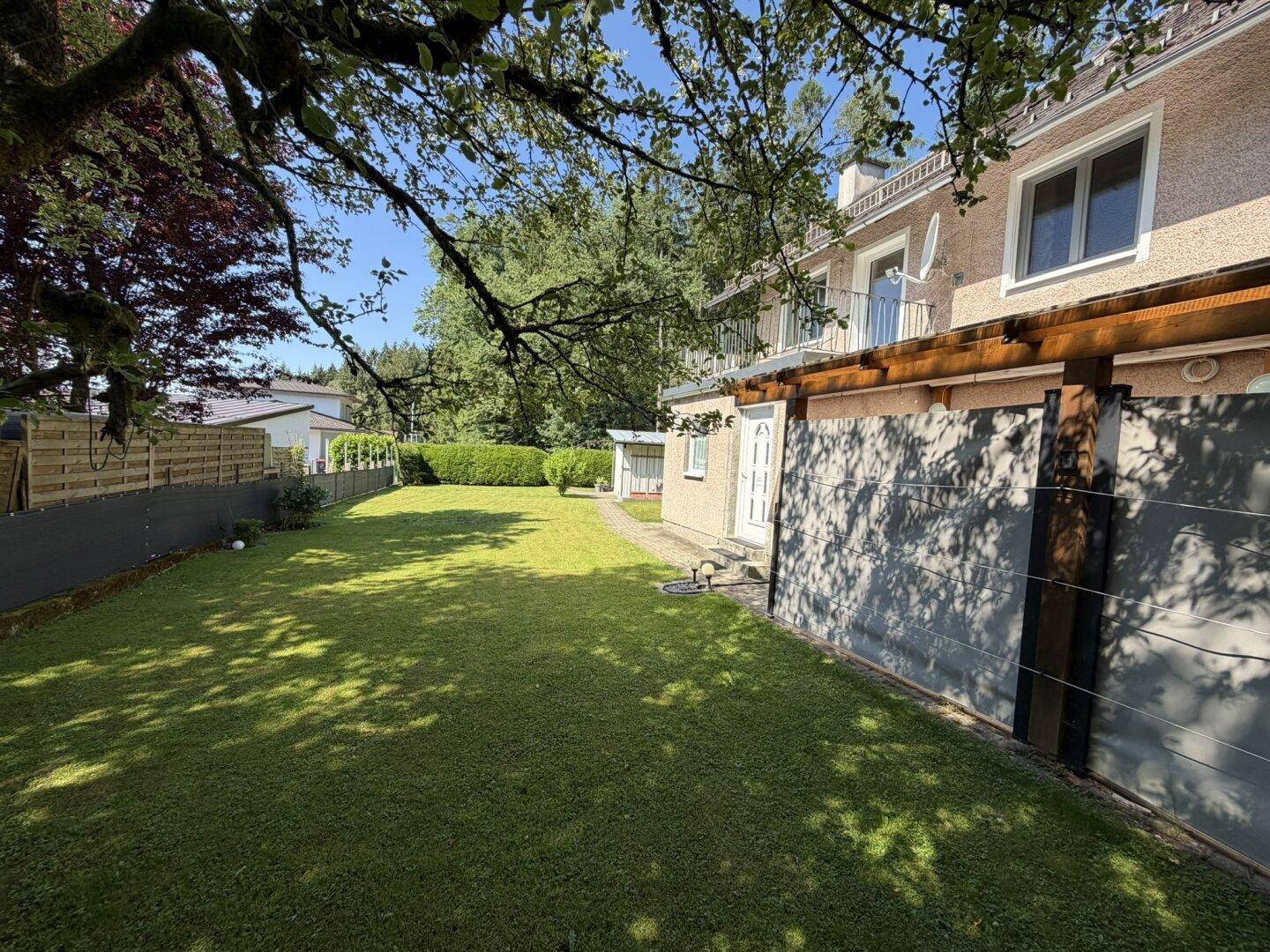 Weitläufiger Gartenbereich mit Rasenfläche und schattenspendenden Bäumen neben dem Haus.