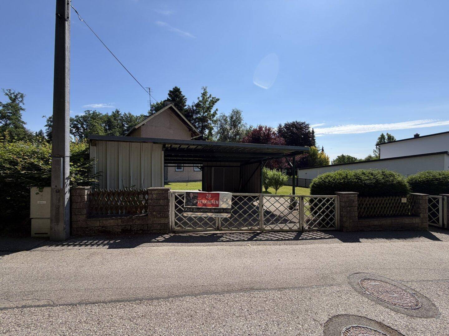 Eingangsbereich des Grundstücks von der Straße aus mit Tor, Zaun und Carport.