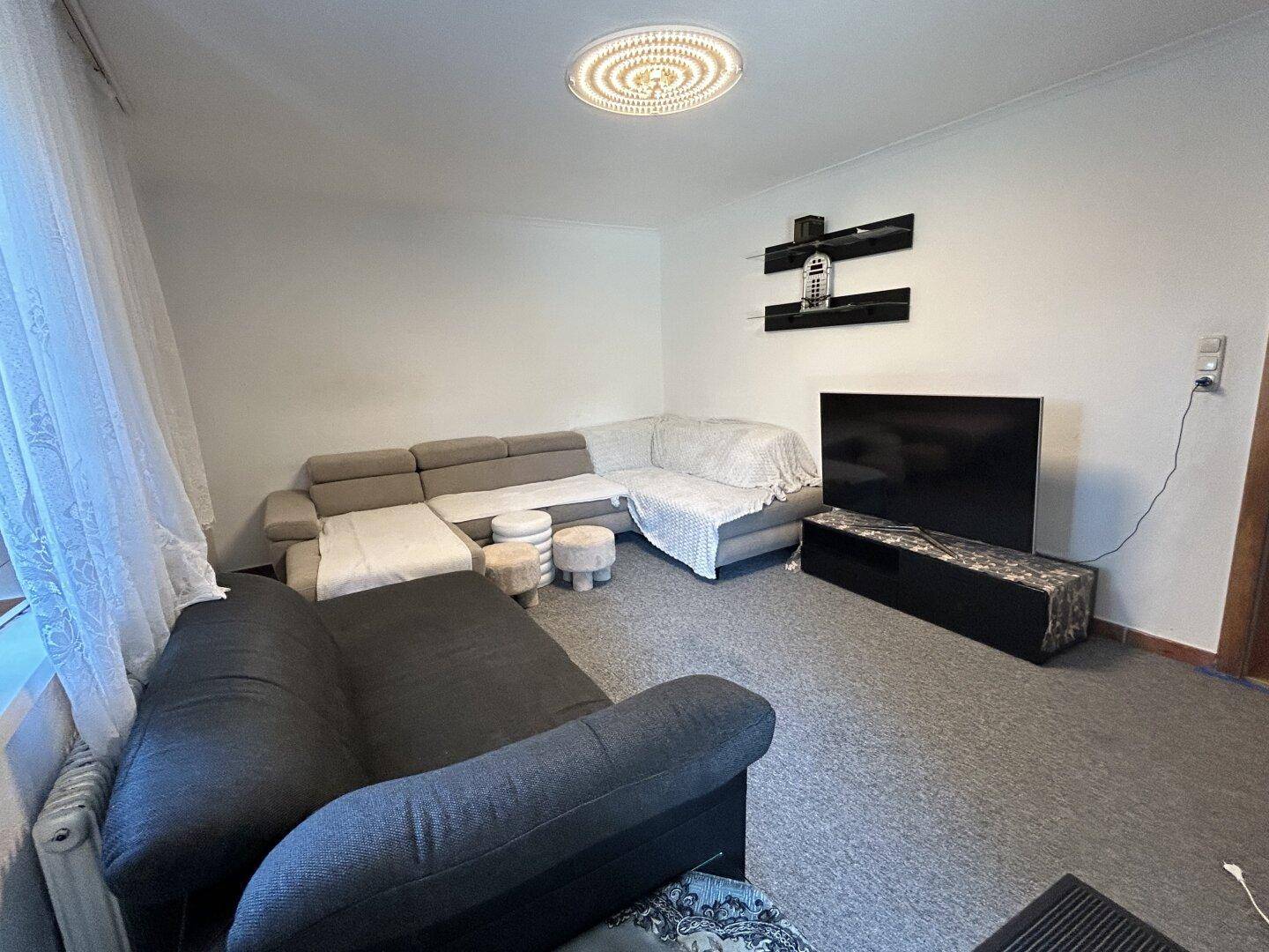 Wohnzimmer mit großem Ecksofa, Teppichboden und einem Fernseher an der Wand.