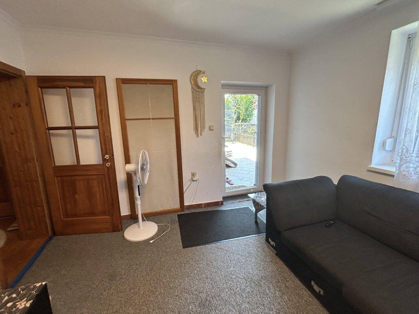 Wohnzimmer mit Sofa und direktem Zugang zu einem sonnigen Außenbereich.