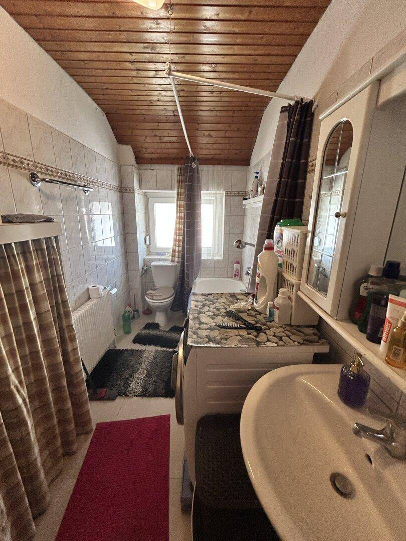 Badezimmer mit Badewanne, Waschbecken, WC und einer rustikalen Holzdecke.