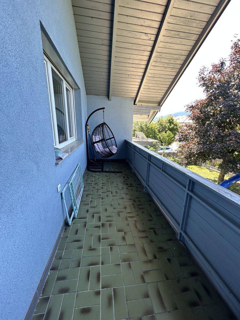 Überdachter Balkon mit Fliesenboden, Hängesessel und Blick ins Grüne.