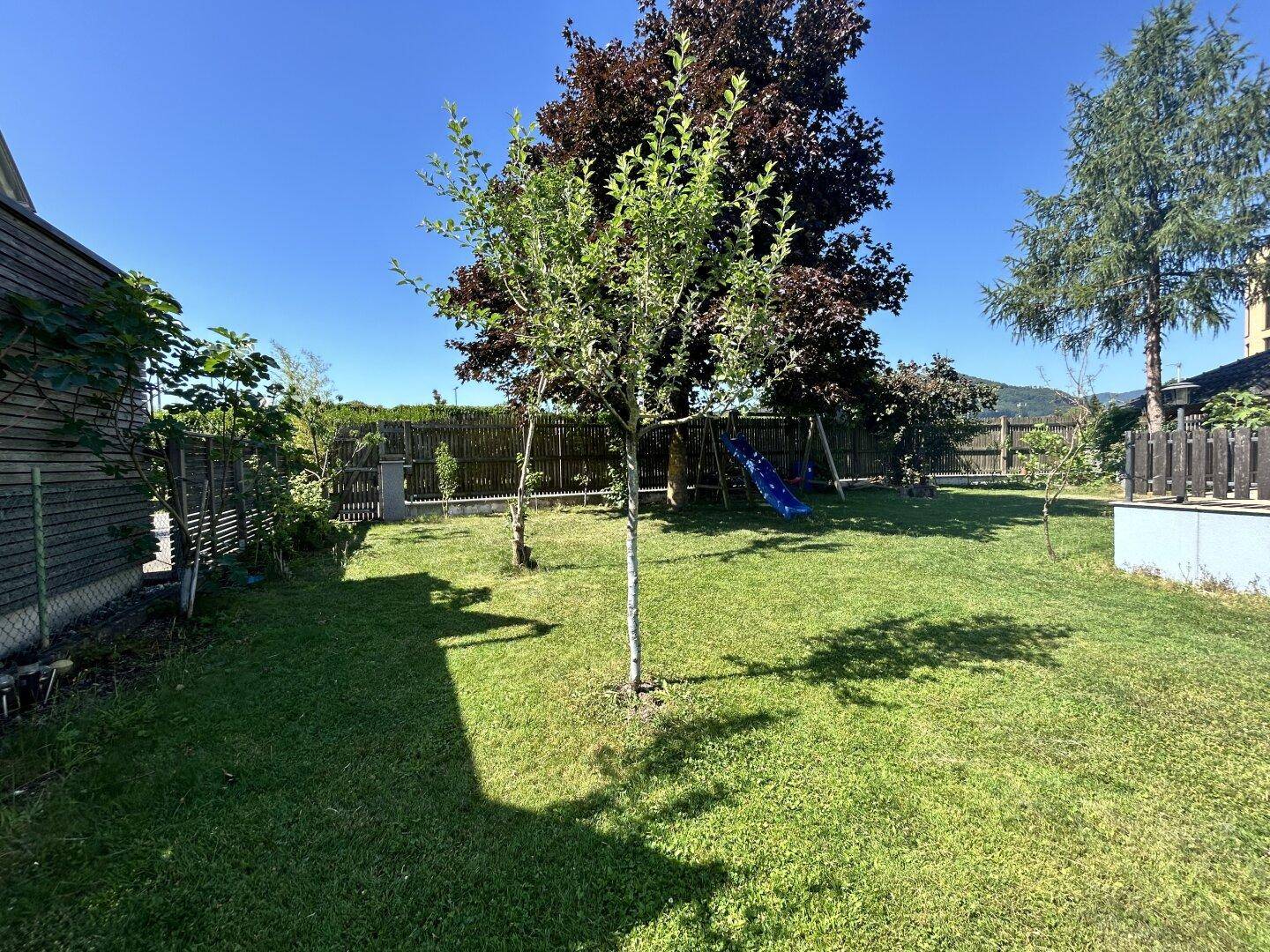 Großer Garten mit Rasenfläche, Bäumen und einem Spielplatz für Kinder.